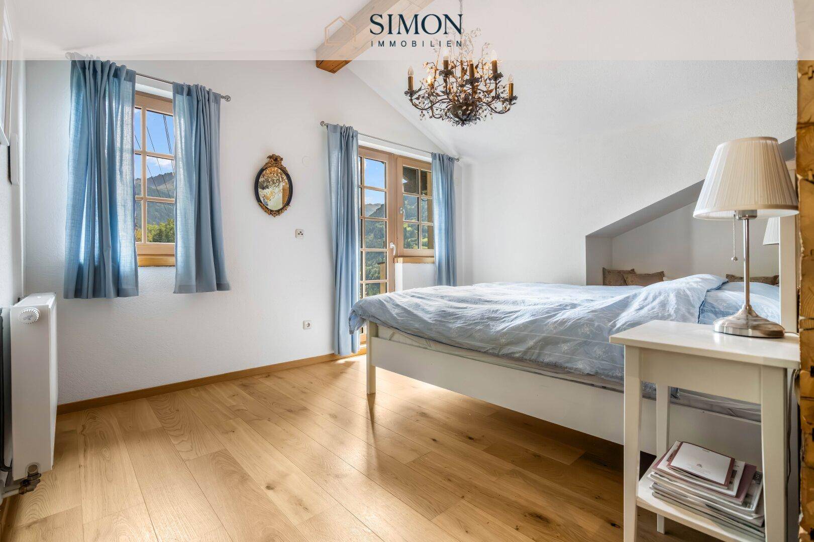 Geräumiges Schlafzimmer mit Holzboden, Doppelbett und Kronleuchter unter Dachschräge.