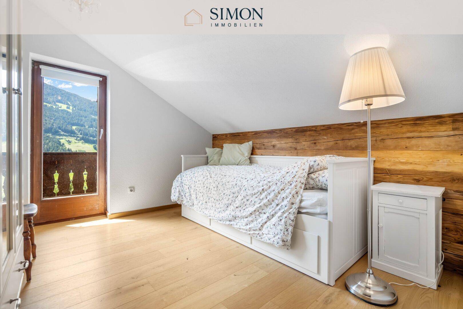 Helles Schlafzimmer mit Holzboden, Einzelbett und Zugang zu einem französischen Balkon mit Bergblick.
