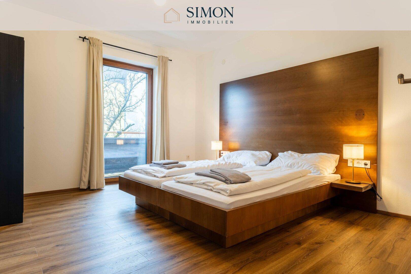 Helles Schlafzimmer mit Holzbett, Laminatboden und großem Fenster mit Blick ins Grüne.