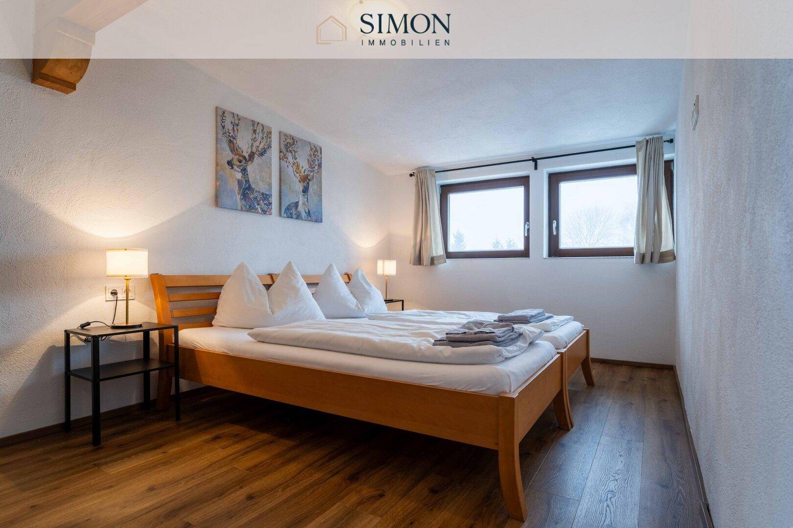 Schlafzimmer mit Holzbett, Laminatboden und zwei Fenstern für eine helle Atmosphäre.