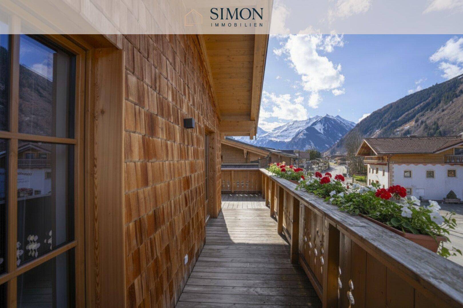 Langer Holzbalkon mit Blumenkästen und weitem Blick auf die umliegende Berglandschaft.