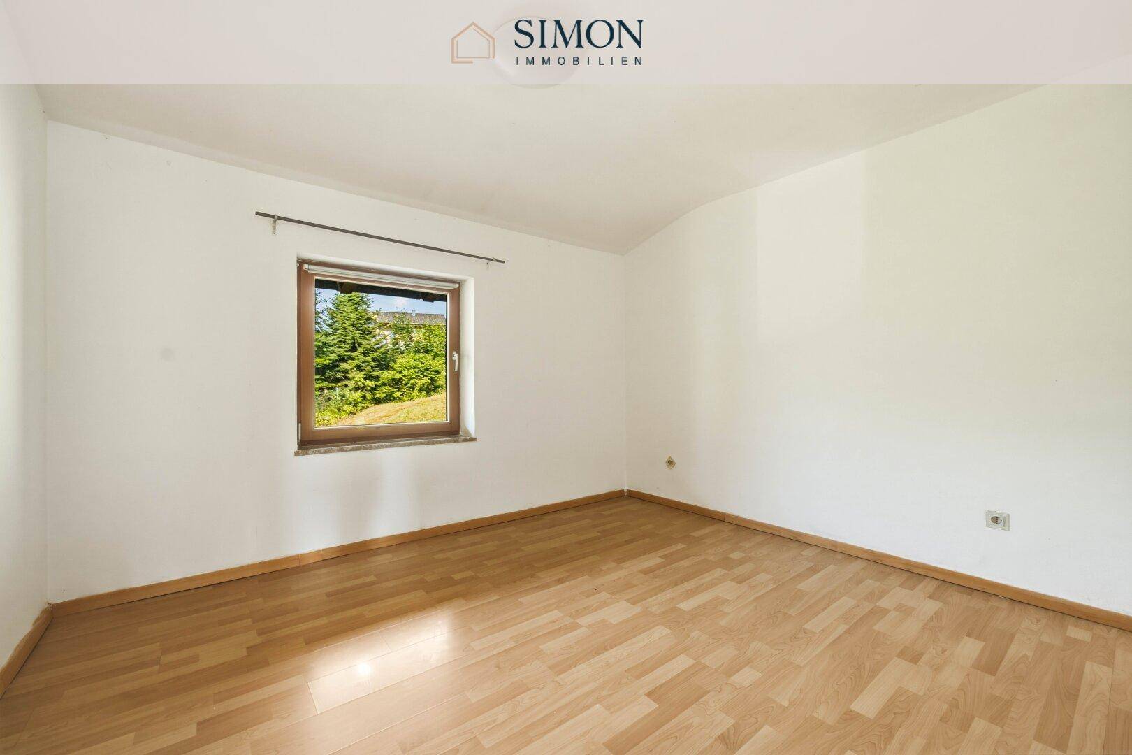 Helles Schlafzimmer mit Holzboden und einem Fenster, das einen Blick ins Grüne bietet.