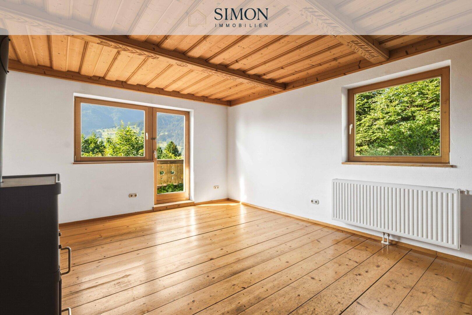 Geräumiges Zimmer mit Holzbalkendecke, Holzdielenboden und Zugang zu einem Balkon.