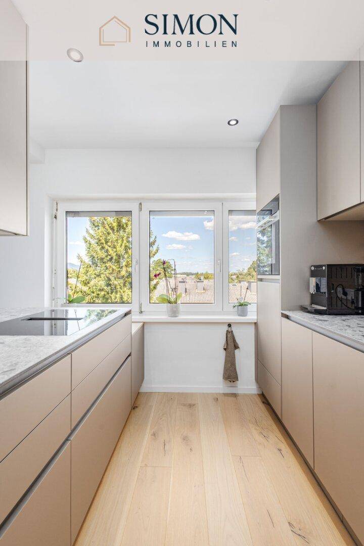 Helle, moderne Küche mit beiger Front, Stein-Arbeitsplatte und Fenster mit Blick nach draußen.