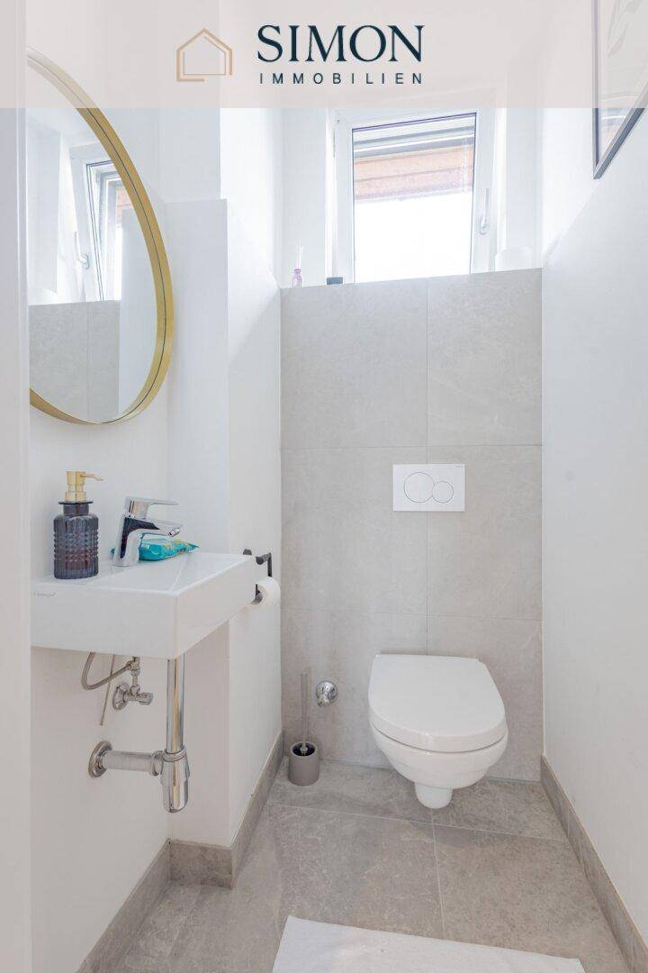 Separates Gäste-WC mit Wand-WC, kleinem Waschbecken und Fenster für natürliche Belüftung.