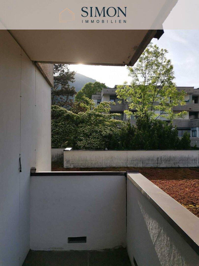 Sonniger Balkon mit Blick auf grüne Bäume und die umliegende Berglandschaft.