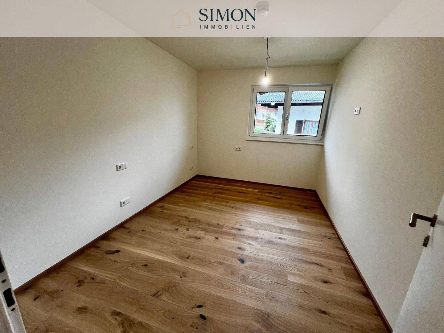 Leeres Zimmer mit hellem Holzfußboden und einem Fenster, ideal als Schlaf- oder Arbeitszimmer.