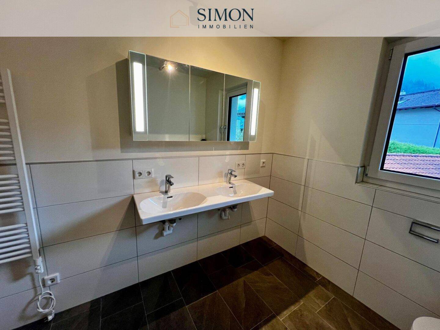 Doppelwaschbecken mit Spiegelschrank, beheiztem Handtuchhalter und Fenster im Badezimmer.