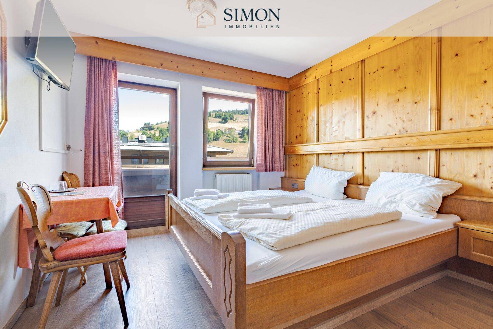 Schlafzimmer mit Holzbett, Holztäfelung und Fenster, das einen Ausblick auf die Umgebung bietet.
