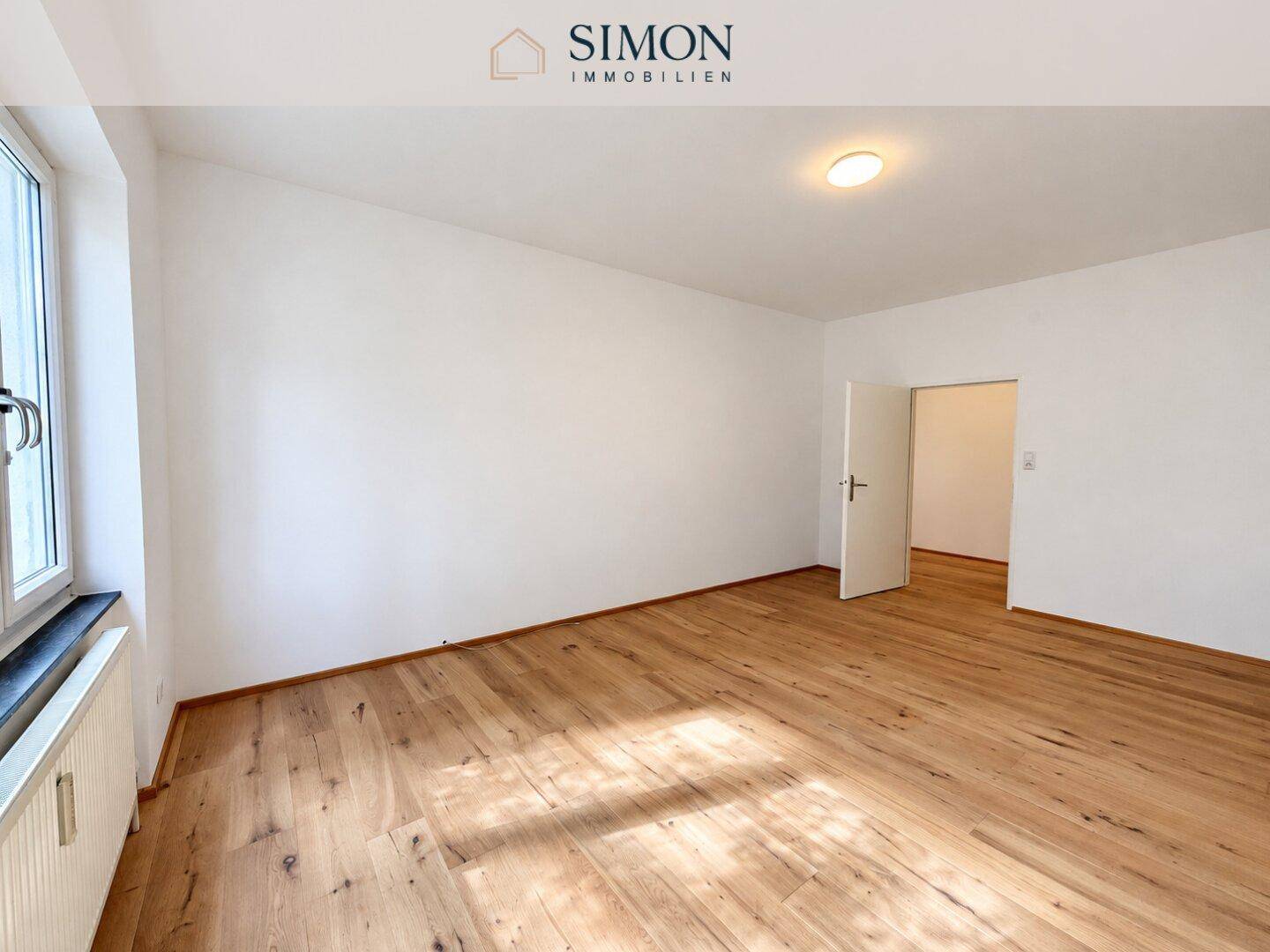 Helles Schlafzimmer mit Holzboden und großem Fenster, ideal für individuelle Einrichtung.