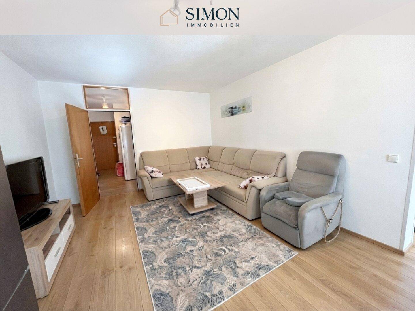 Gemütliches Wohnzimmer mit Ecksofa, Sessel und Holzboden, ideal zum Entspannen.
