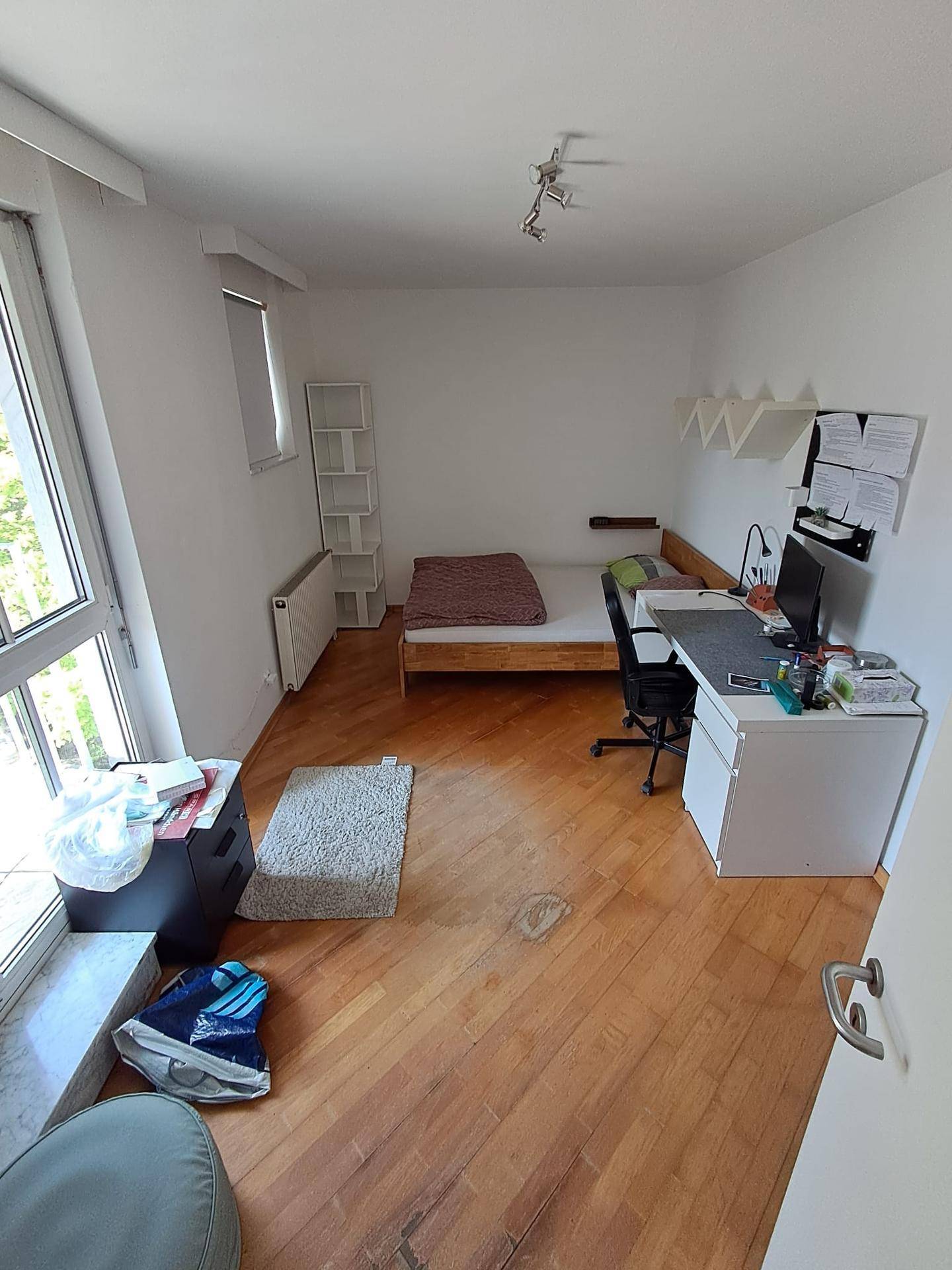 Gemütliches Schlafzimmer mit Holzboden, Bett, Schreibtisch und viel Tageslicht durch große Fenster.