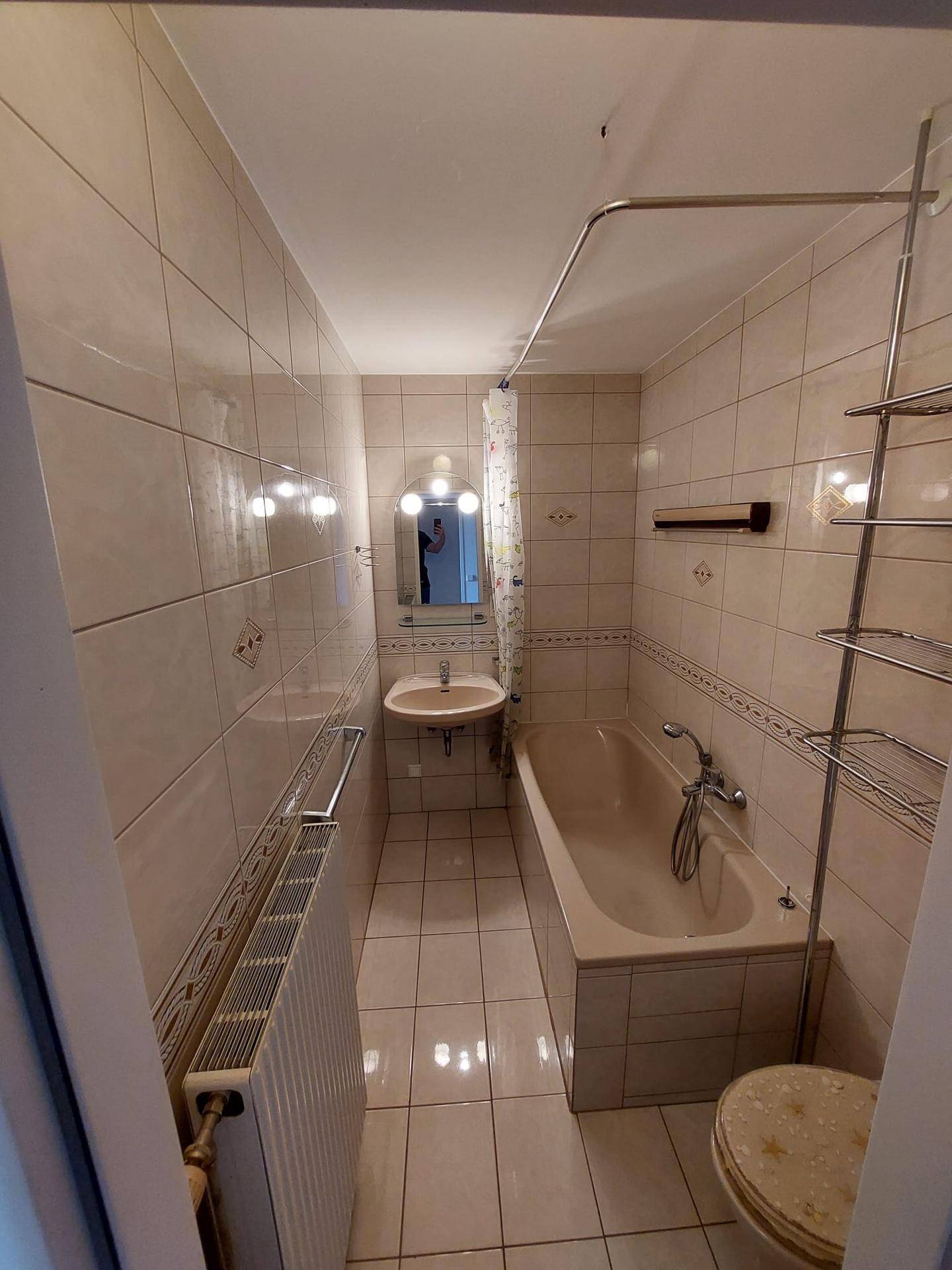 Gefliestes Badezimmer mit Badewanne, Duschvorhang, Waschbecken und Toilette in beigen Farbtönen.
