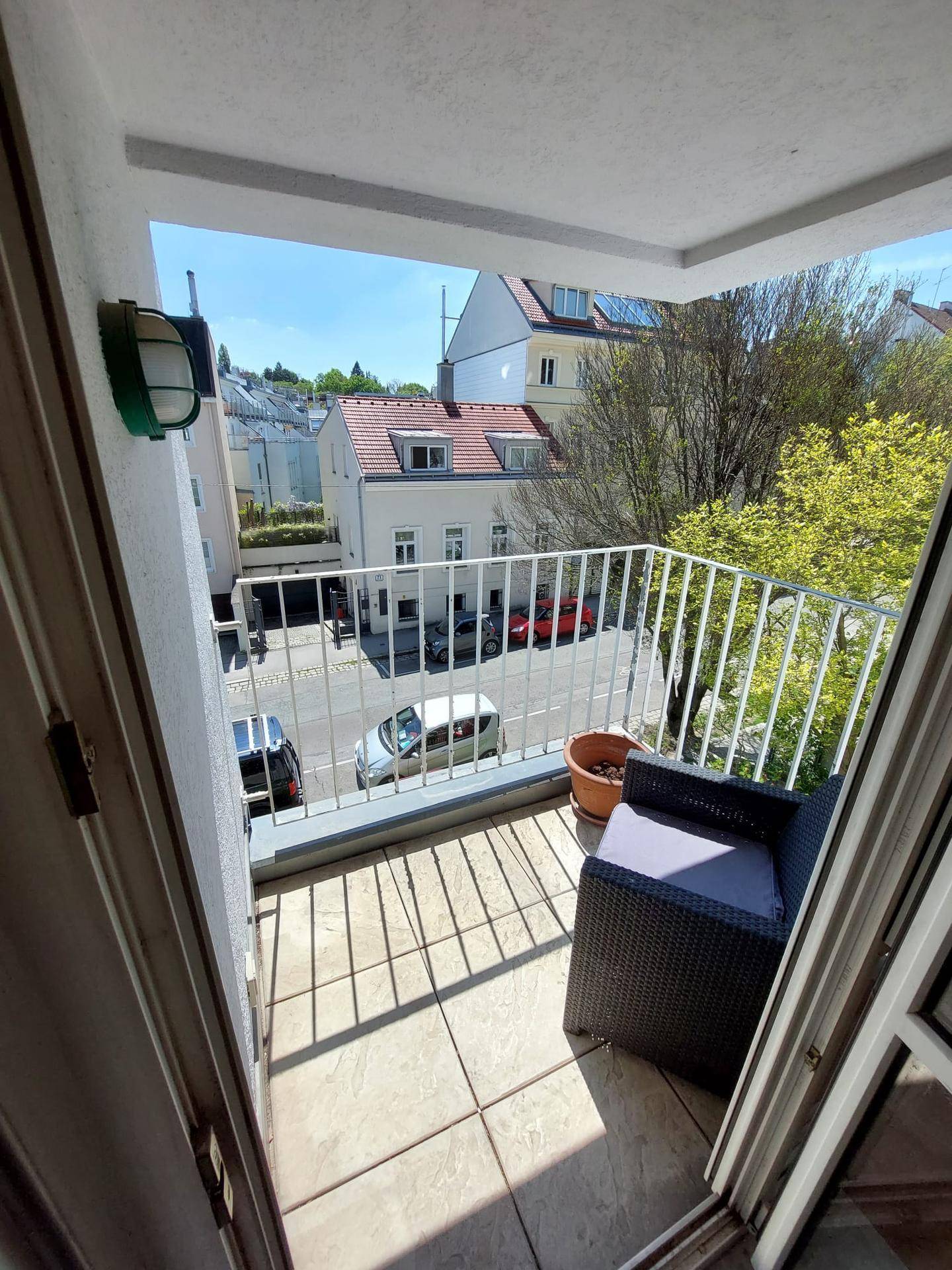 Kleiner Balkon mit Sitzgelegenheit und Blick auf die Straße sowie umliegende Gebäude und Bäume.