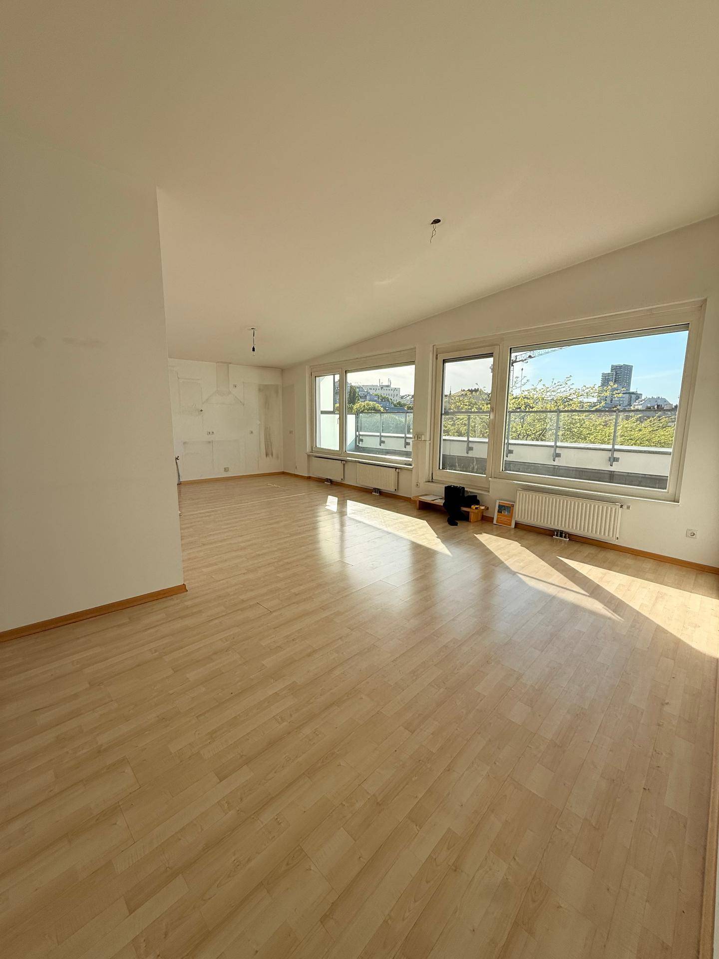Helles Wohnzimmer mit Laminatboden und großen Fenstern, die viel Tageslicht hereinlassen.
