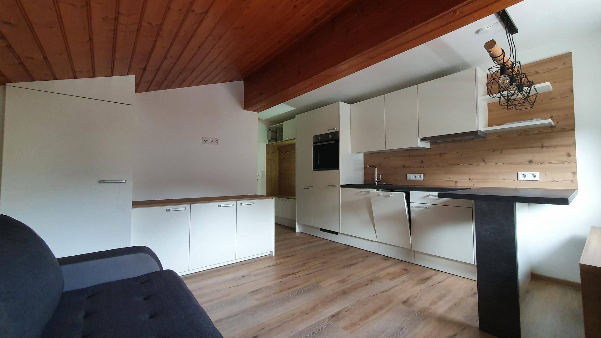 Heller Wohnbereich mit Sofa, integrierter Küche und Garderobenbereich unter der Holzdachschräge.