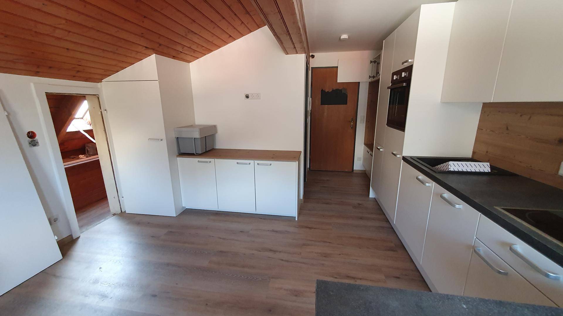 Helle Küche mit weißen Schränken, Holzwandverkleidung und Dachschrägen in einem offenen Grundriss.