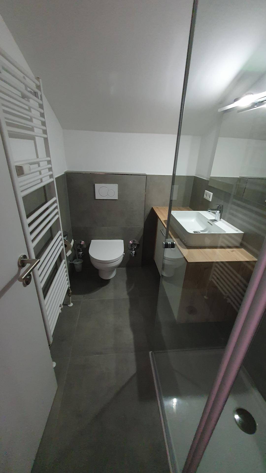 Modernes Badezimmer mit grauen Fliesen, wandhängendem WC, Einzelwaschbecken und begehbarer Dusche.