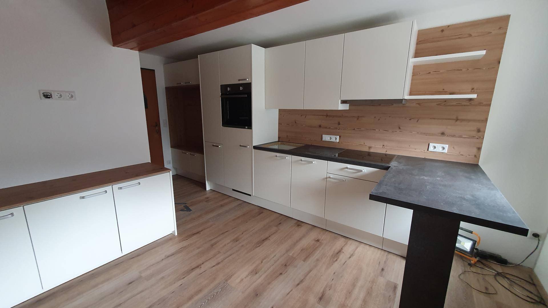 Moderne Einbauküche mit weißen Fronten, dunkler Arbeitsplatte und Holzakzenten im offenen Wohnbereich.