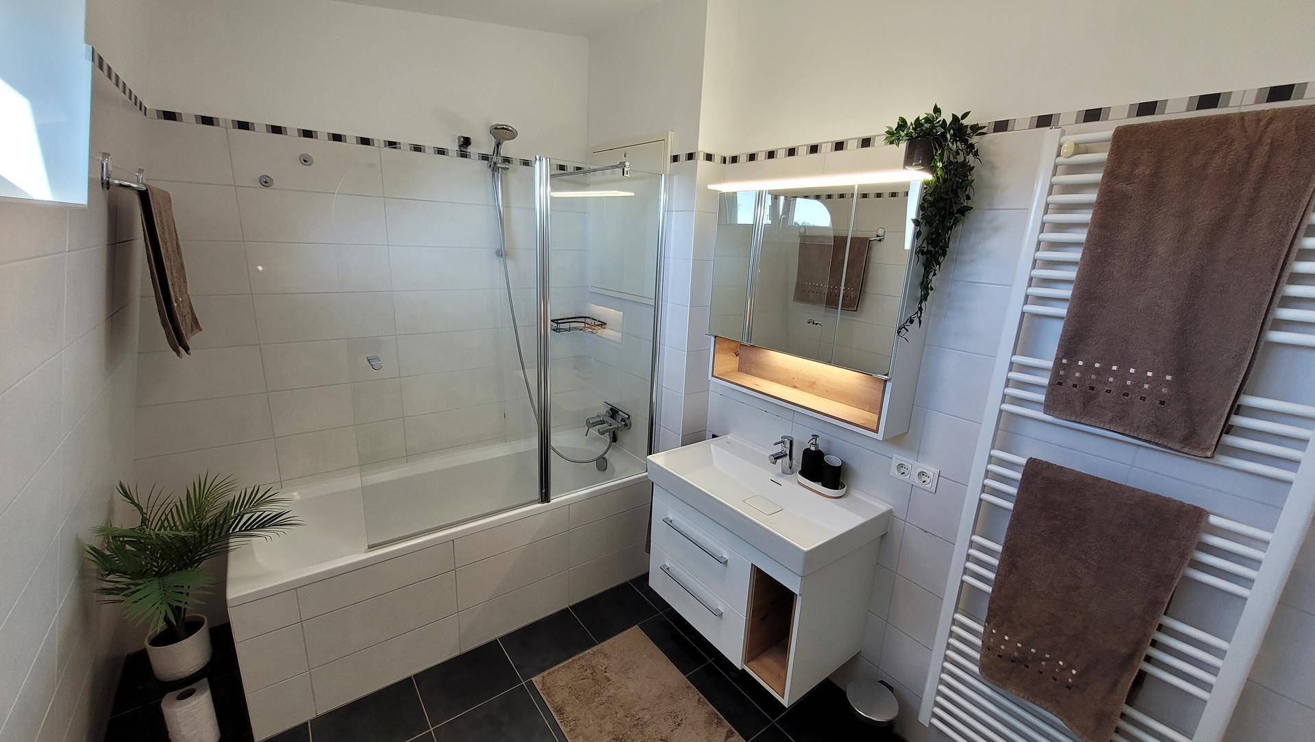 Funktionales Badezimmer mit Badewanne, Duschabtrennung, Waschtisch und praktischem Handtuchheizkörper.