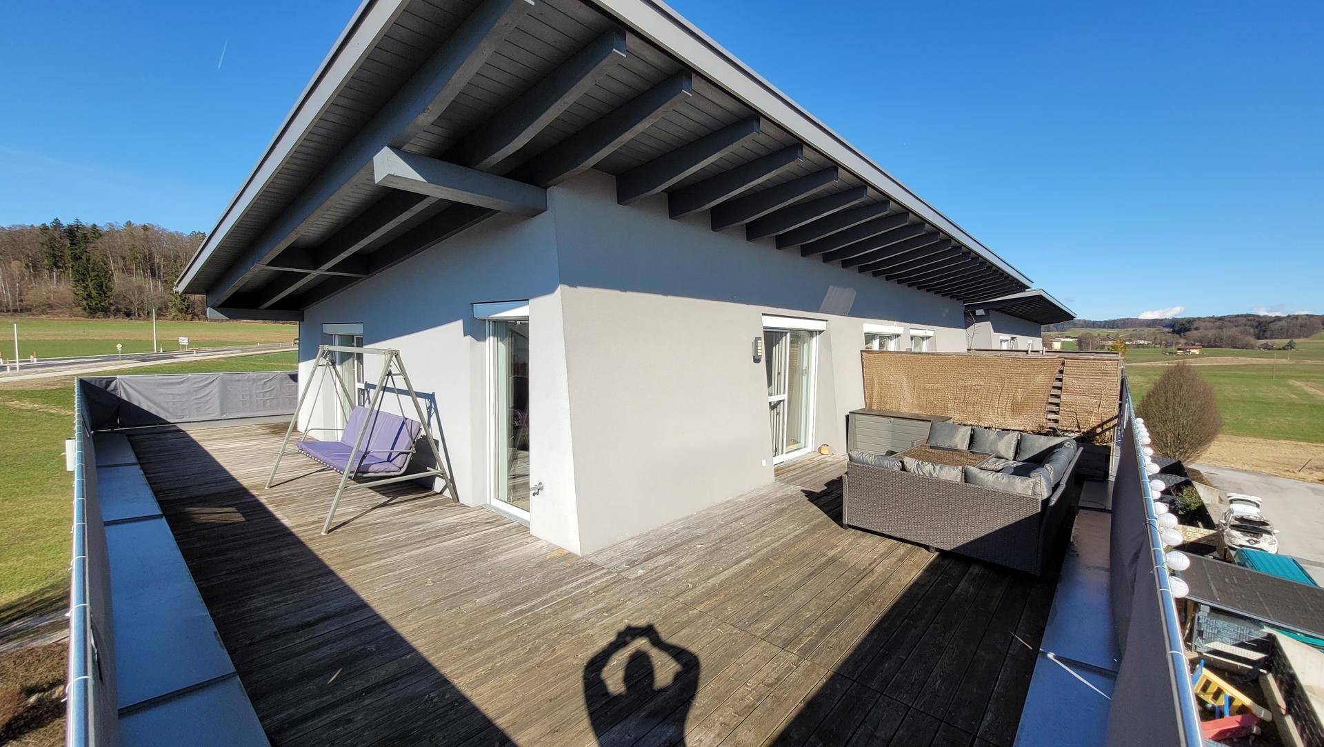 Weitläufige Terrasse mit Holzboden, Schaukel und Blick auf die umliegende grüne Landschaft.