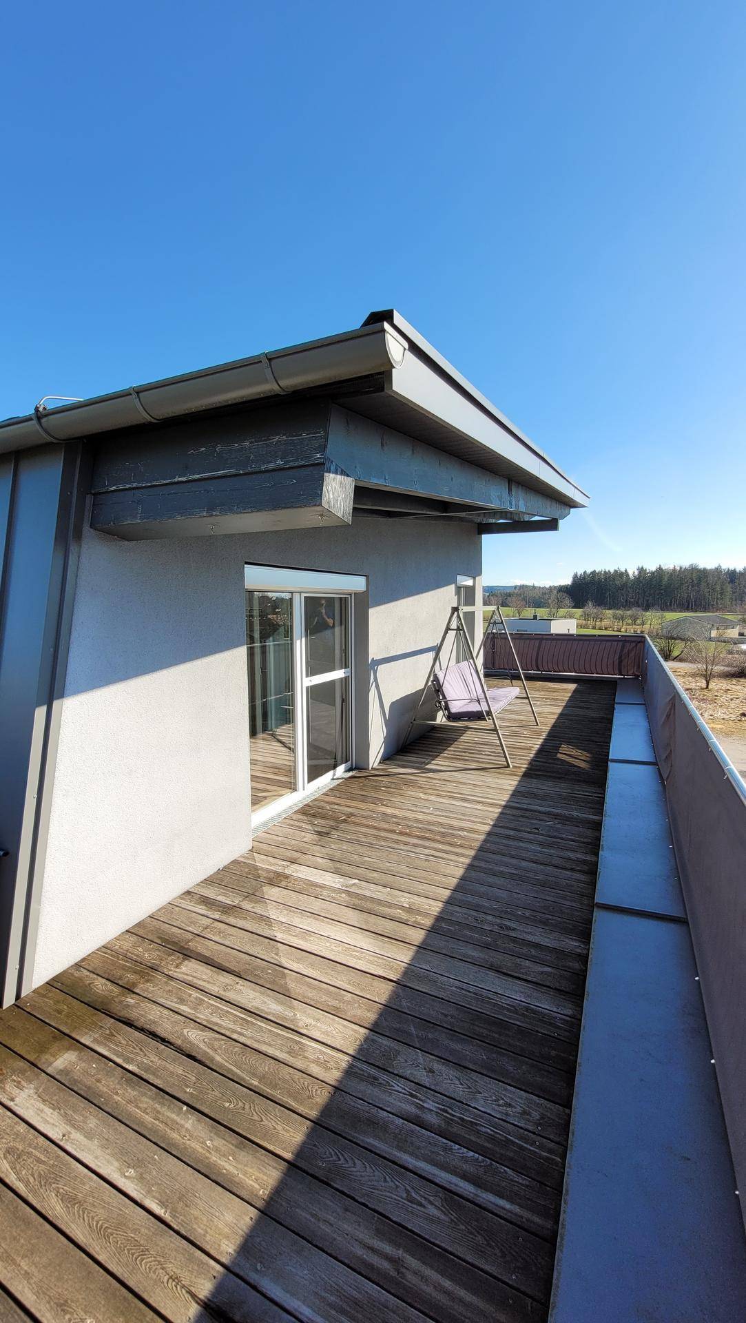 Sonnige Terrasse mit Holzdielenboden und einer Schaukel, ideal zum Entspannen im Freien.