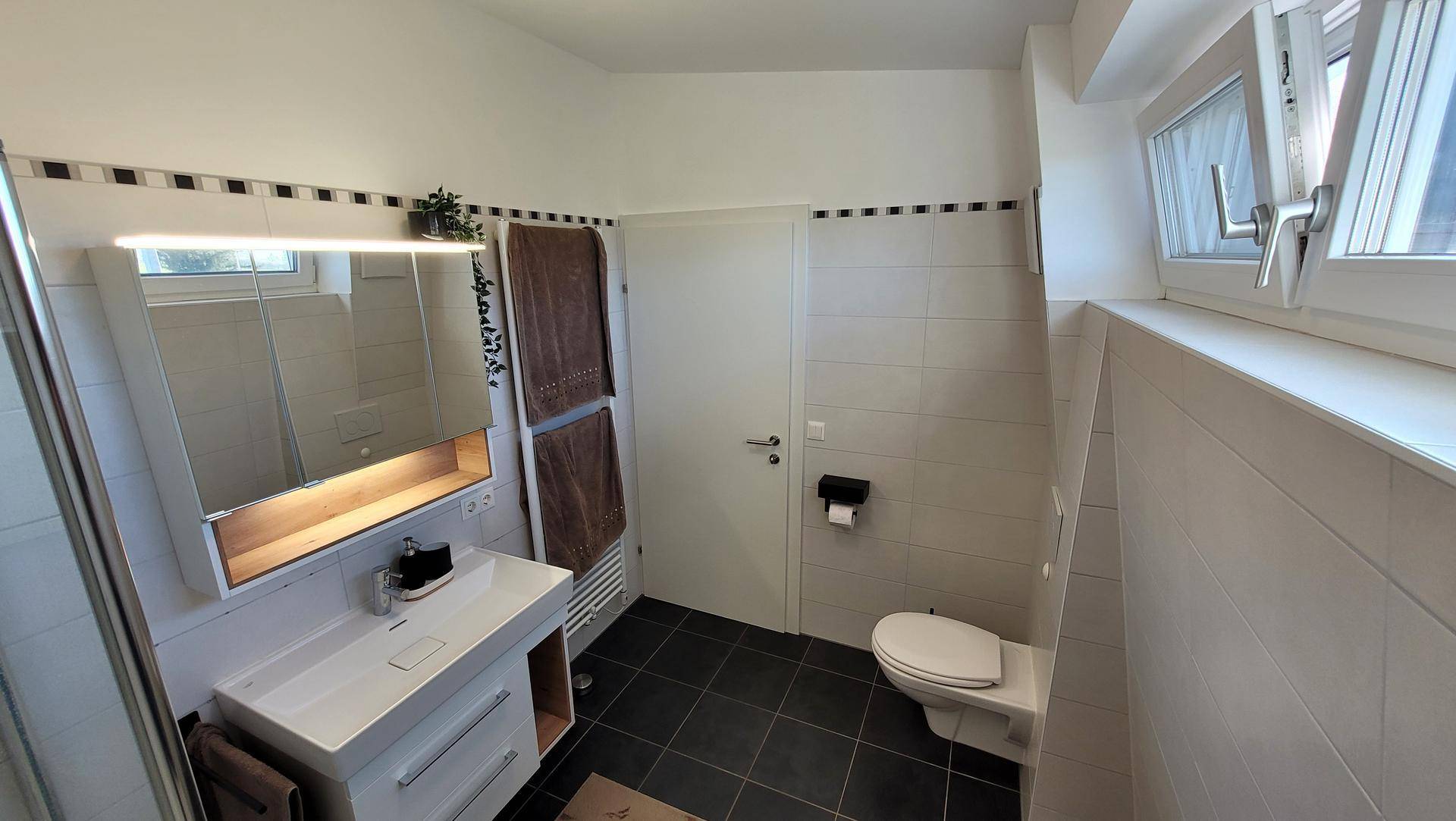 Modernes Badezimmer mit Waschtisch, Spiegelschrank, WC und beheiztem Handtuchhalter.