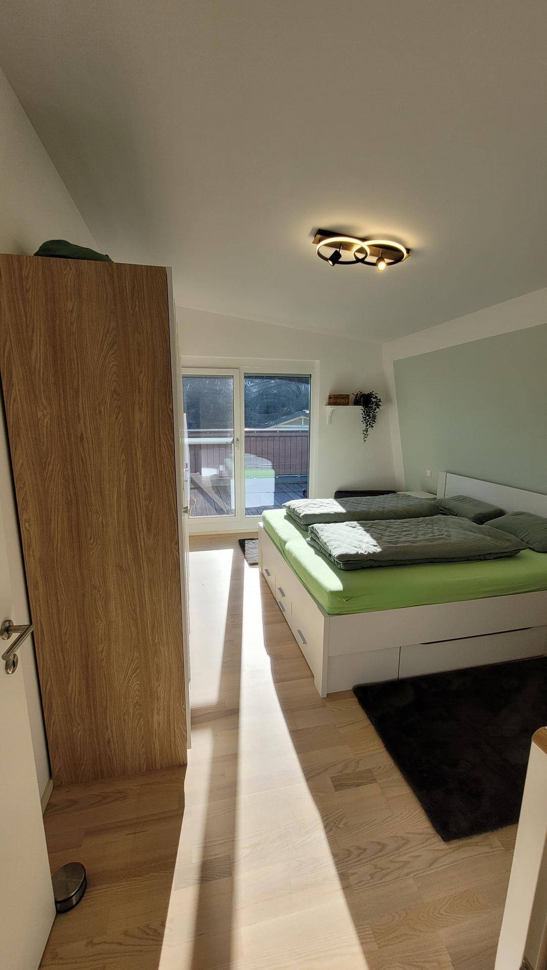 Helles Schlafzimmer mit Doppelbett, Kleiderschrank und Zugang zu einem kleinen Außenbereich.