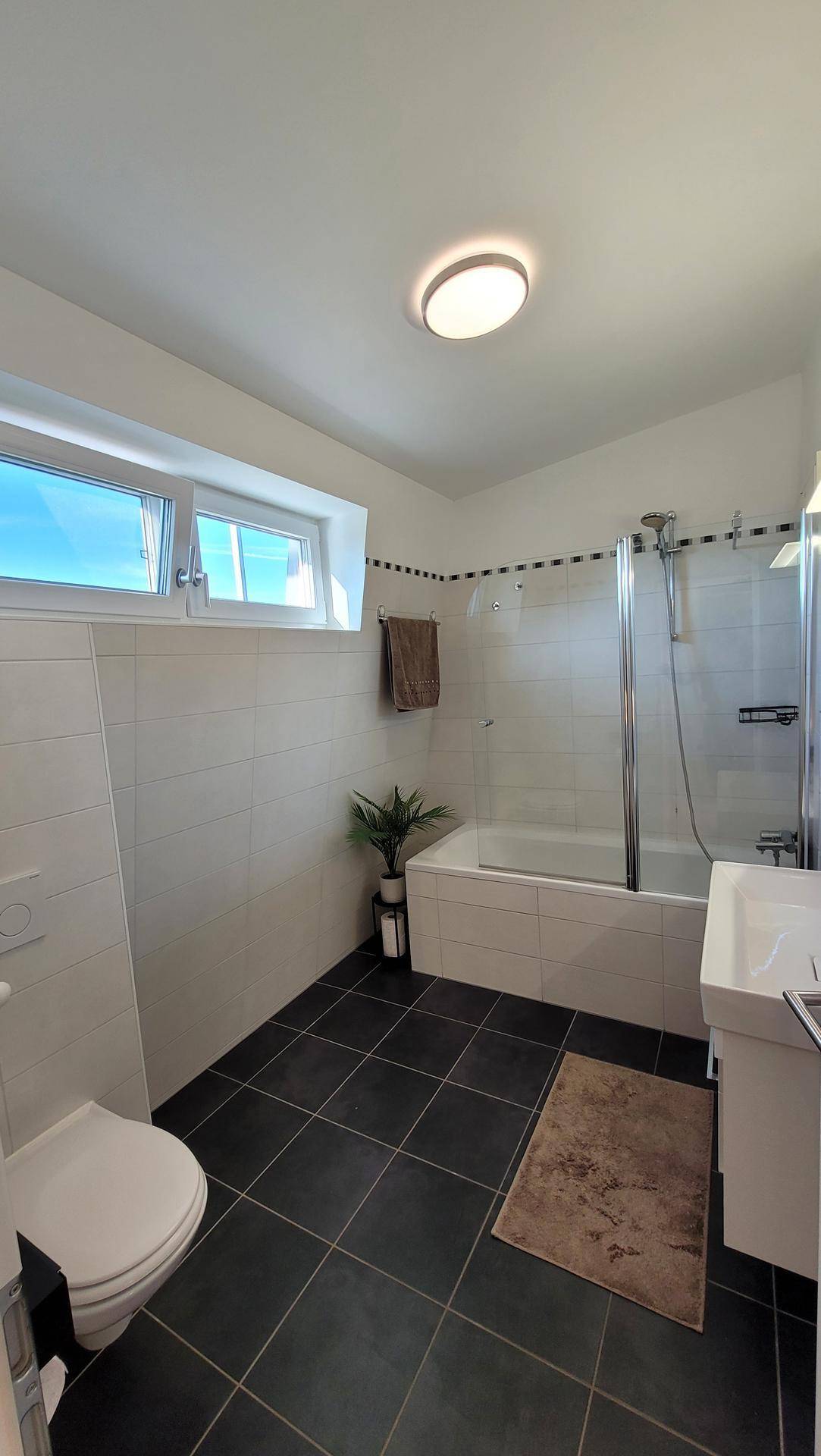 Helles Badezimmer mit Badewanne, Dusche, WC und Fenster für natürliche Belüftung.