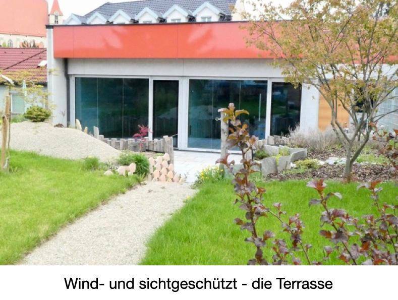 Wind- und sichtgeschützte Terrasse mit großen Glasfronten und einem kleinen Gartenbereich.