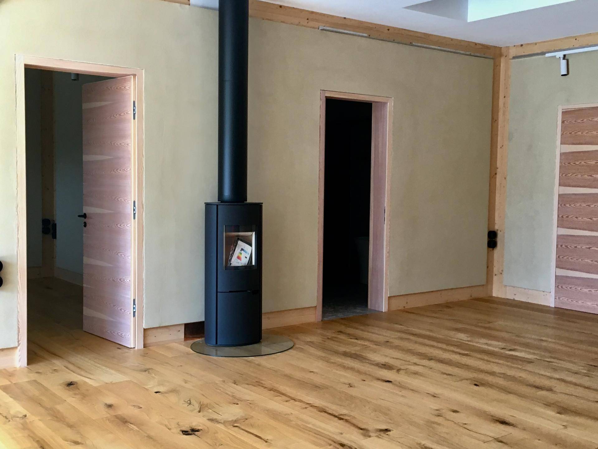 Heller Wohnraum mit Holzboden, beigen Wänden und einem modernen freistehenden Kaminofen.