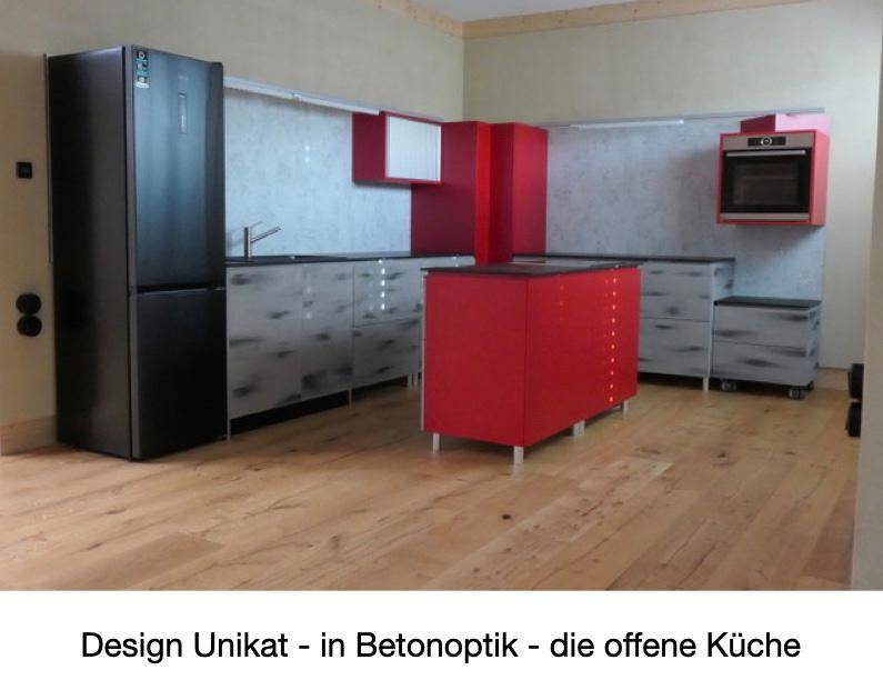 Offene Designküche in Betonoptik mit roten Akzenten, schwarzem Kühlschrank und Holzfußboden.