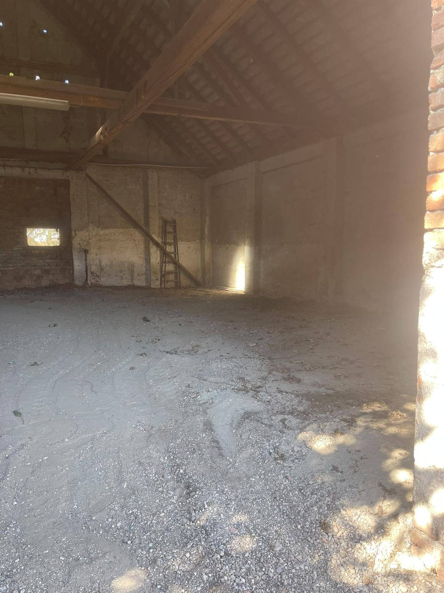 Weitläufiger Innenraum einer Lagerhalle mit Holzdachkonstruktion und einem hellen Lichteinfall.