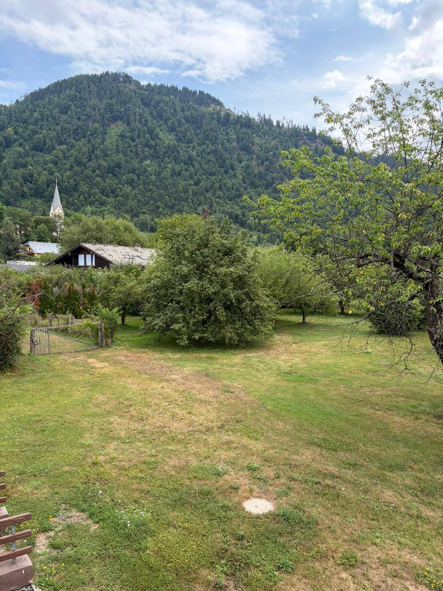 Weitläufiger Gartenbereich mit altem Baumbestand und Blick auf die umliegende Berglandschaft und Kirche.