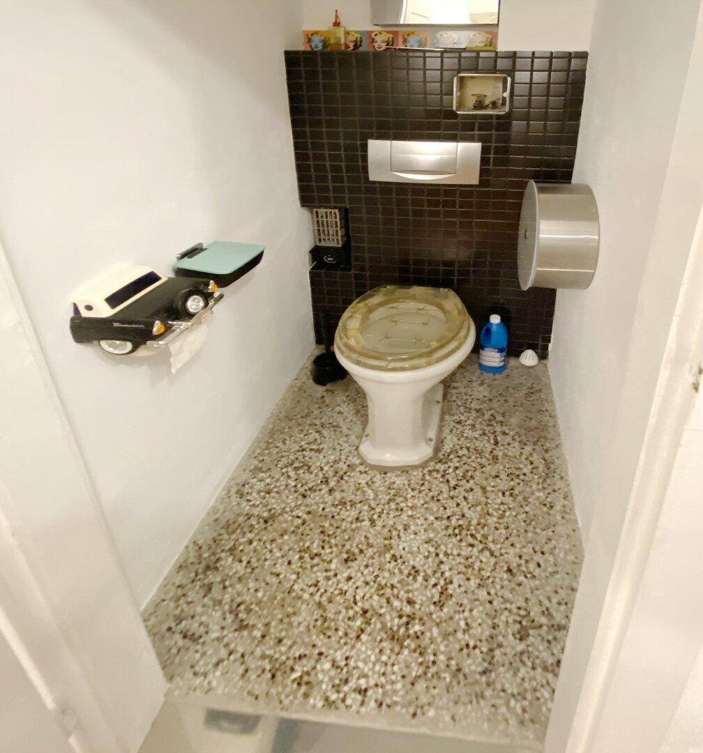 Kleine Gästetoilette mit dunklen Fliesen und einem Terrazzoboden, funktional eingerichtet.