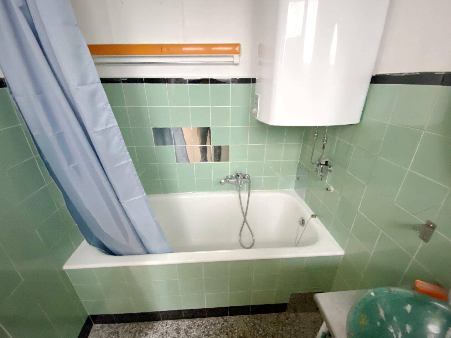 Badezimmer mit Badewanne, mintgrünen Fliesen und Duschvorhang.