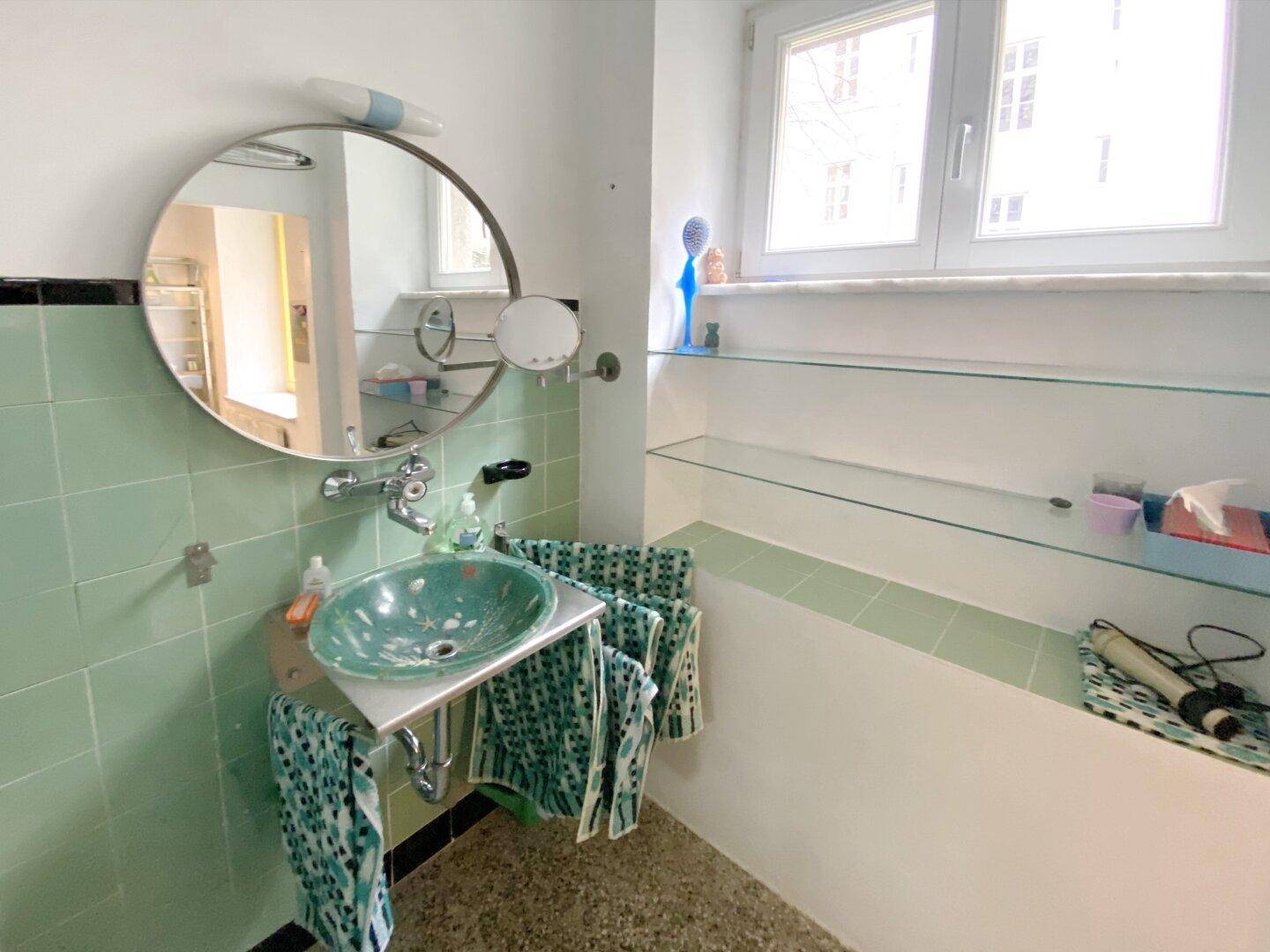 Badezimmer mit mintgrünen Fliesen, modernem Waschbecken und Fenster.