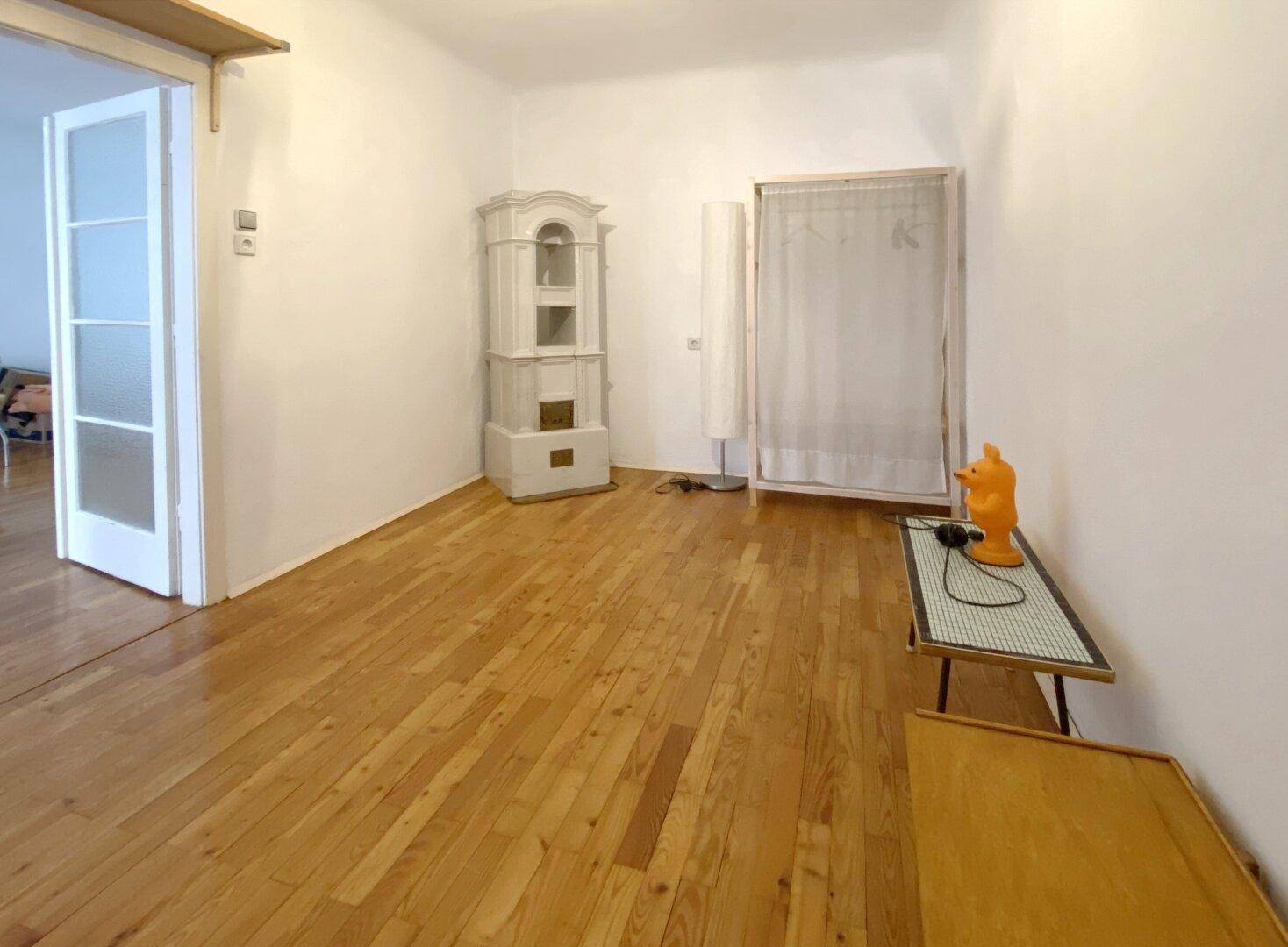 Geräumiges Zimmer mit Holzboden und einem traditionellen Kachelofen als Heizelement.