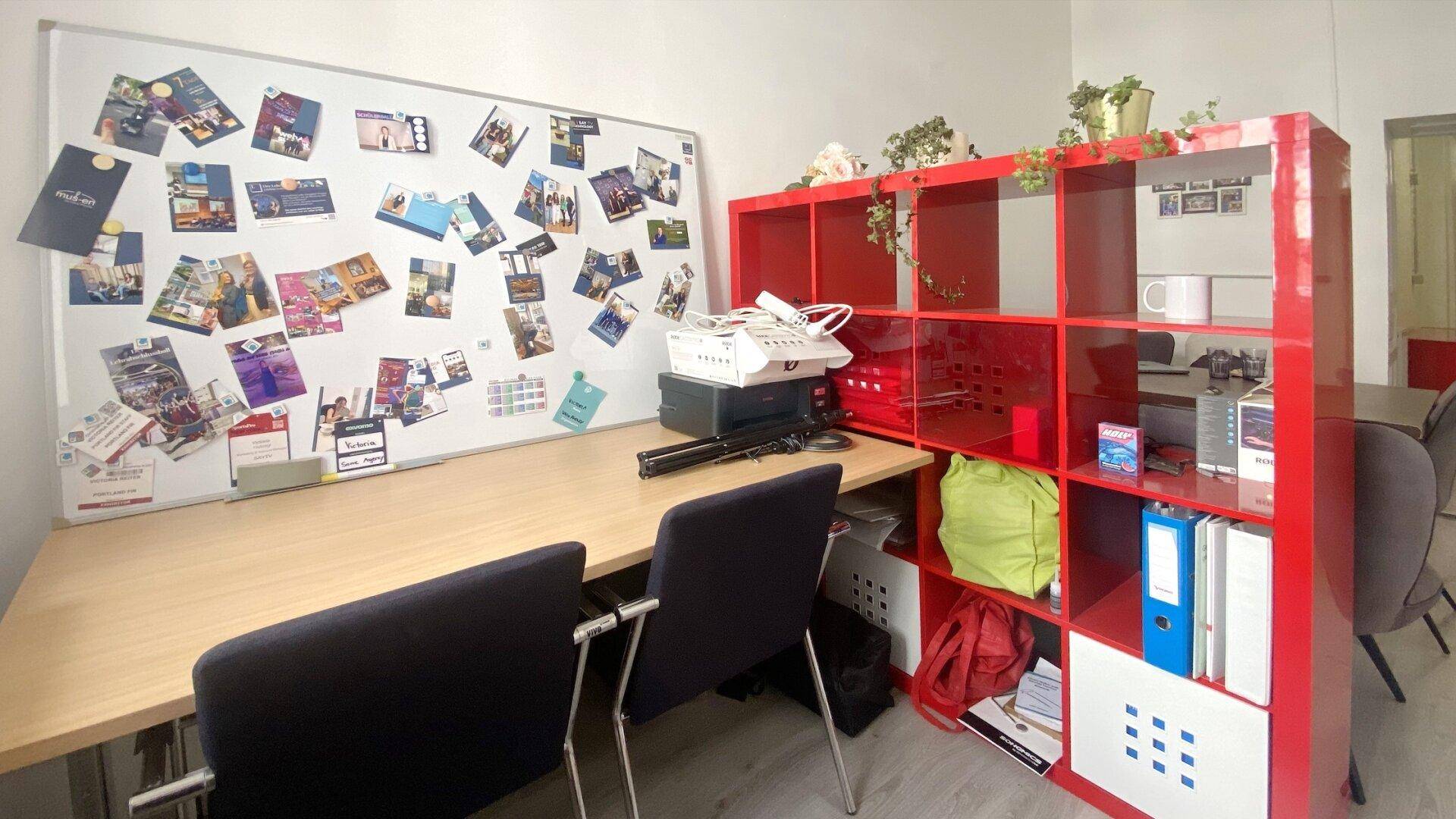 Arbeitsbereich mit einem großen Whiteboard, einem roten Regal und zwei Bürostühlen, ideal für Teamarbeit.