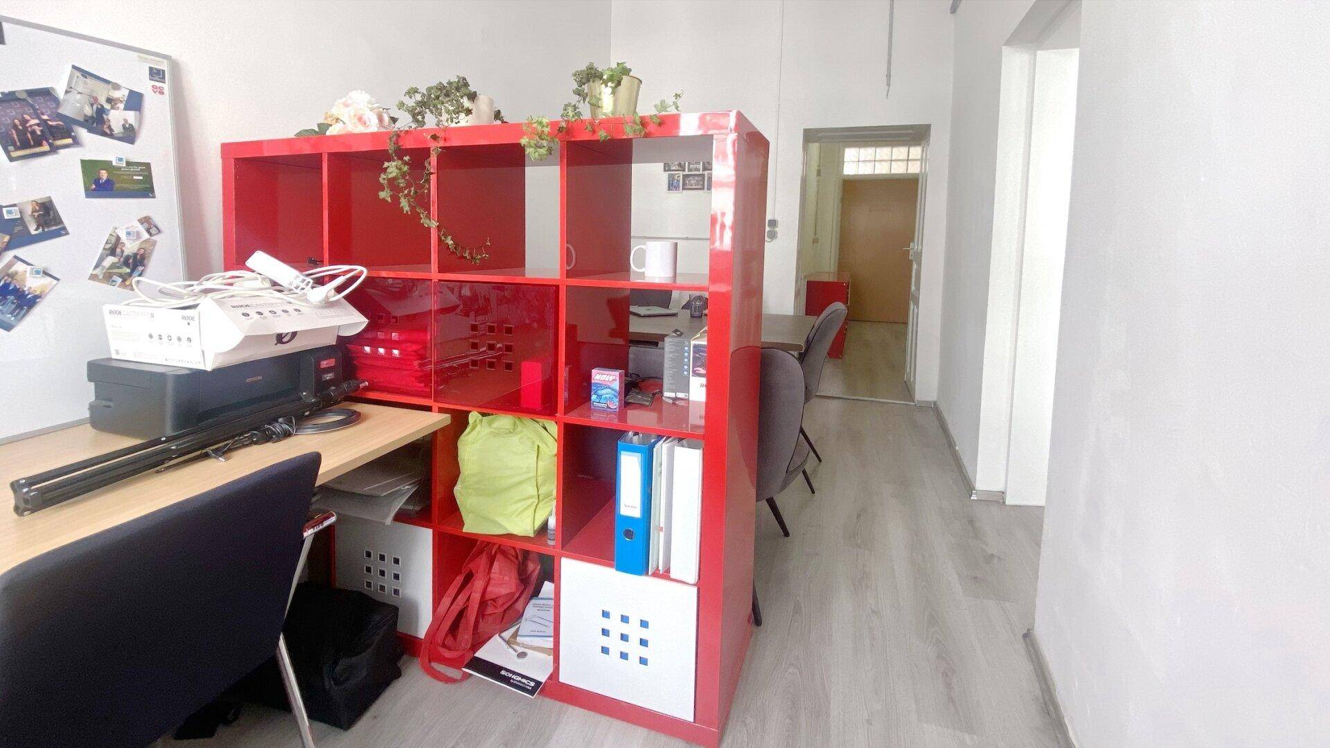 Rotes Regal in einem Büroraum mit Whiteboard und Blick auf einen Flur, der zu weiteren Bereichen führt.