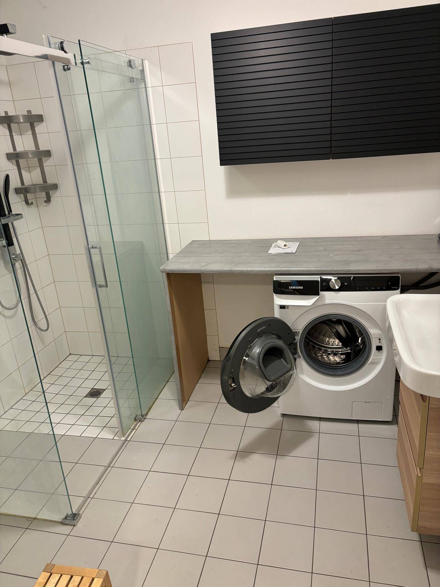 Funktionaler Waschraum mit Dusche, Waschmaschine und praktischer Arbeitsfläche.