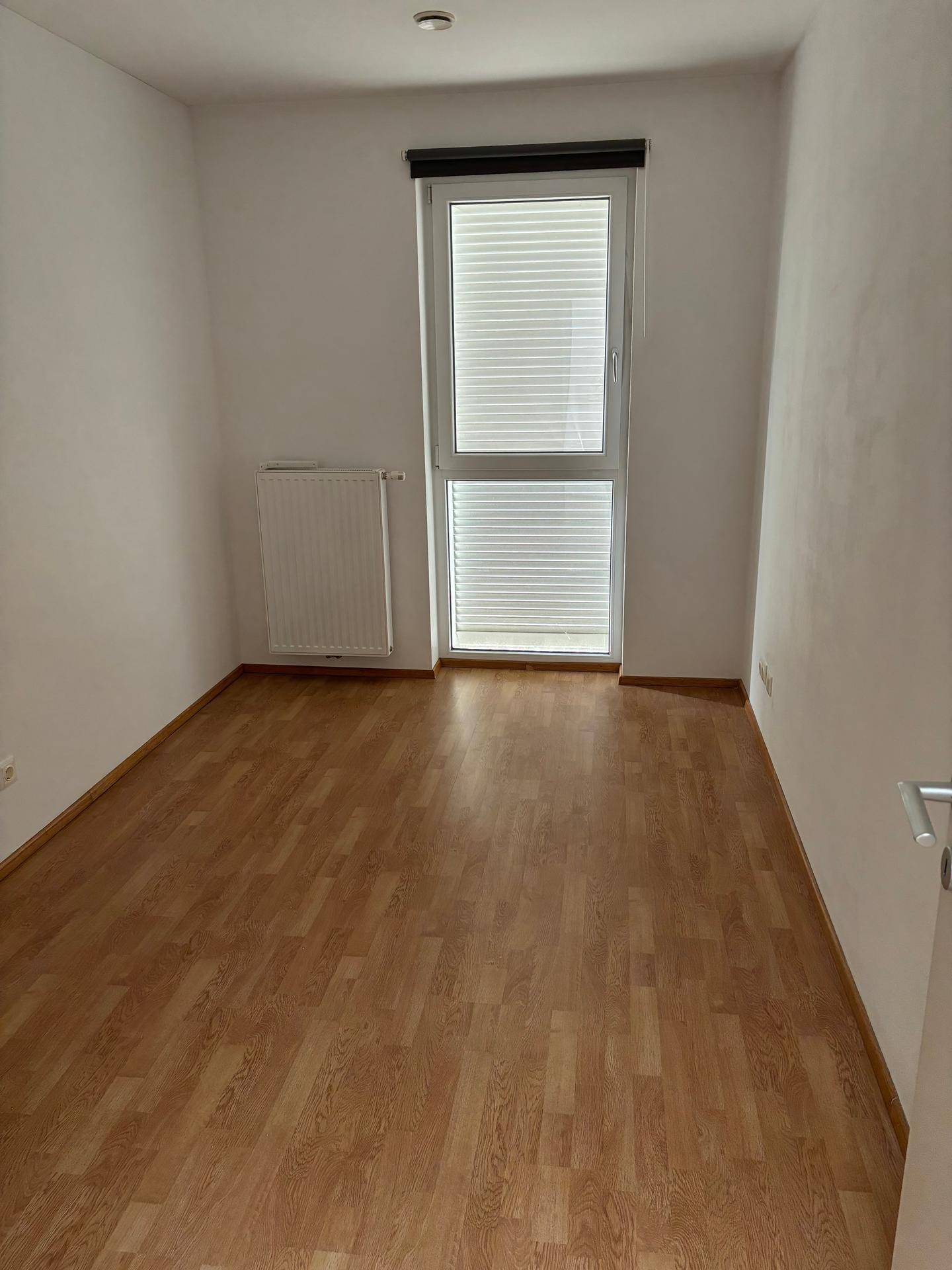 Gemütliches Zimmer mit Laminatboden und Fenster, das viel Tageslicht hereinlässt.