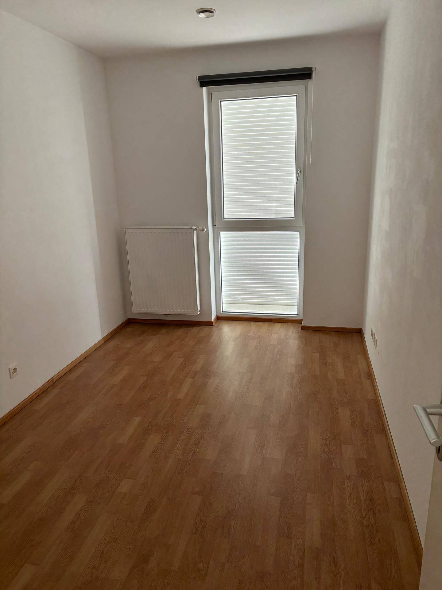 Schlafzimmer mit Laminatboden, Fenster mit Jalousien und Heizkörper, ideal für Ruhe und Erholung.