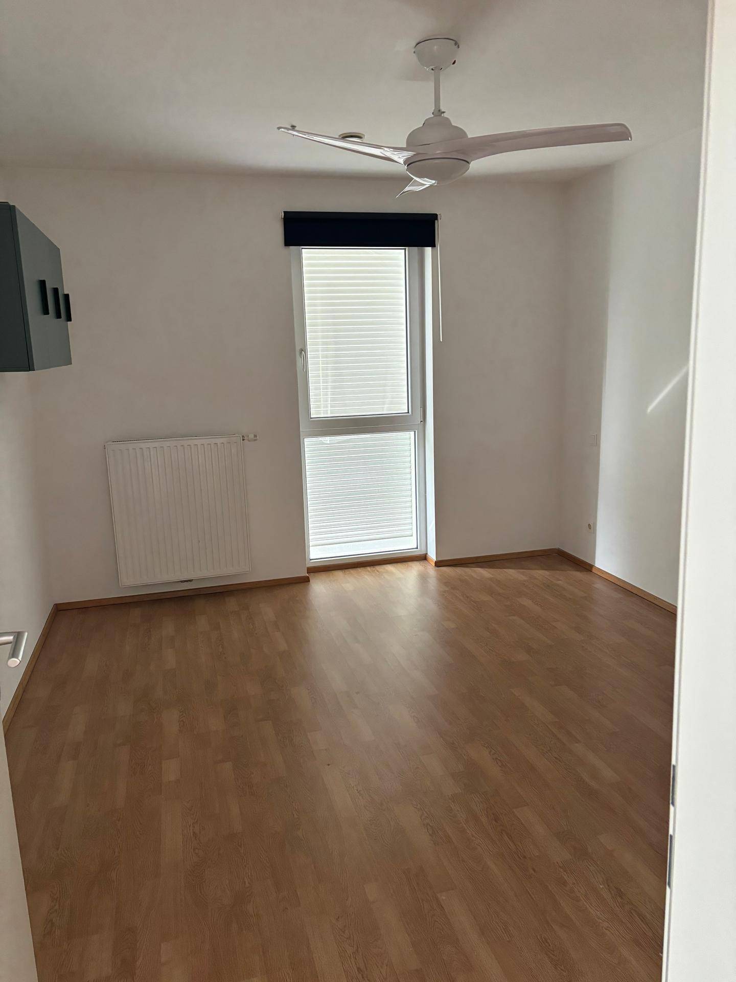 Helles Zimmer mit Laminatboden, Fenster und Deckenventilator für angenehme Temperaturen.