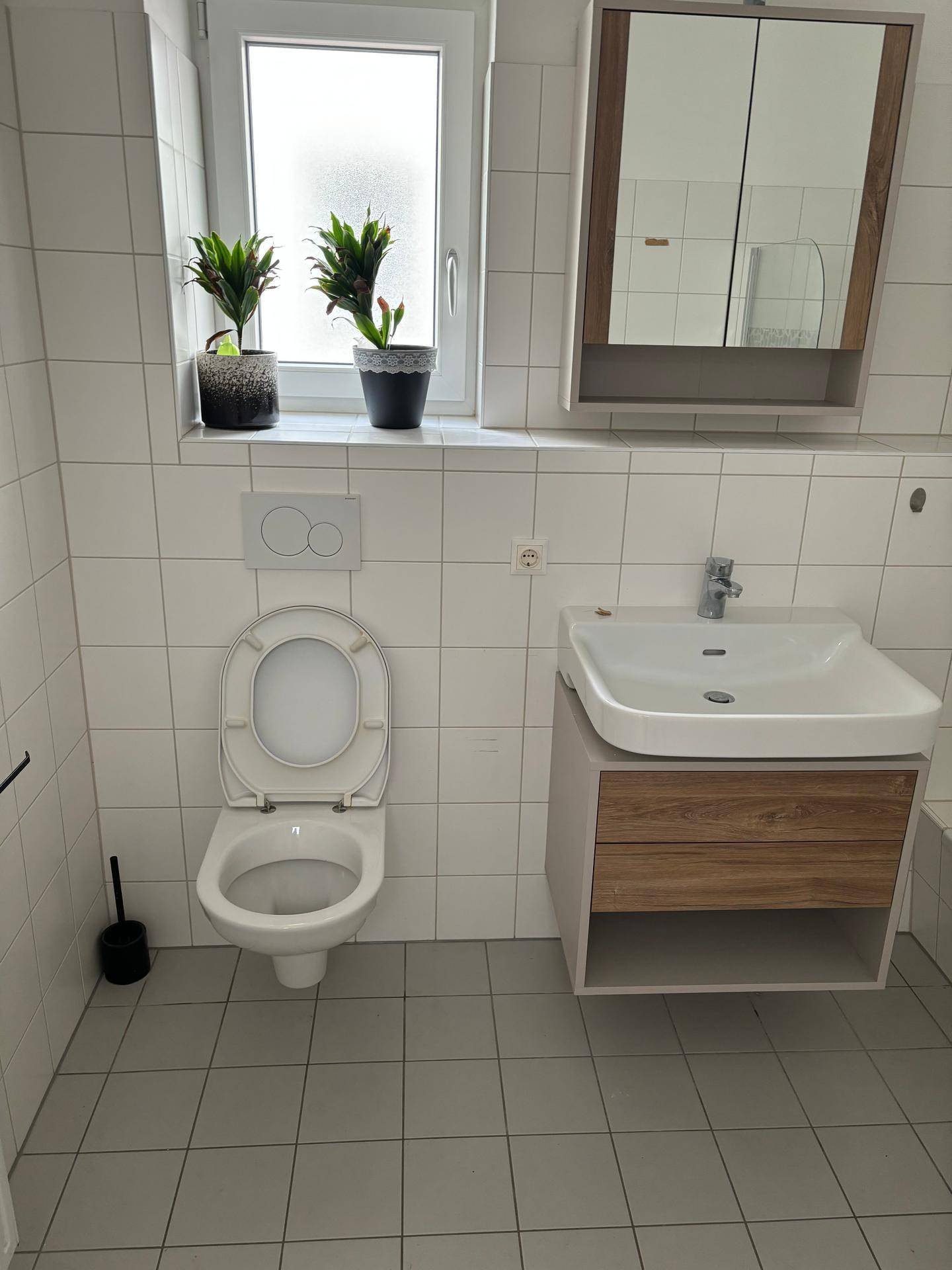 Badezimmer mit WC, Waschtisch, Spiegelschrank und Fenster für natürliche Belüftung.