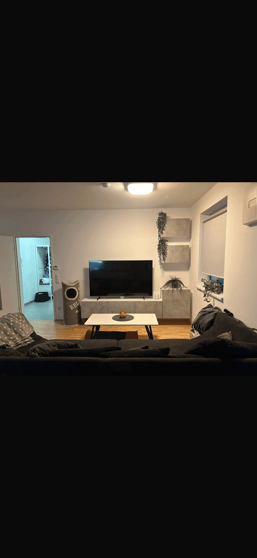 Gemütliches Wohnzimmer mit großem Fernseher, modernen Möbeln und hellem Parkettboden.
