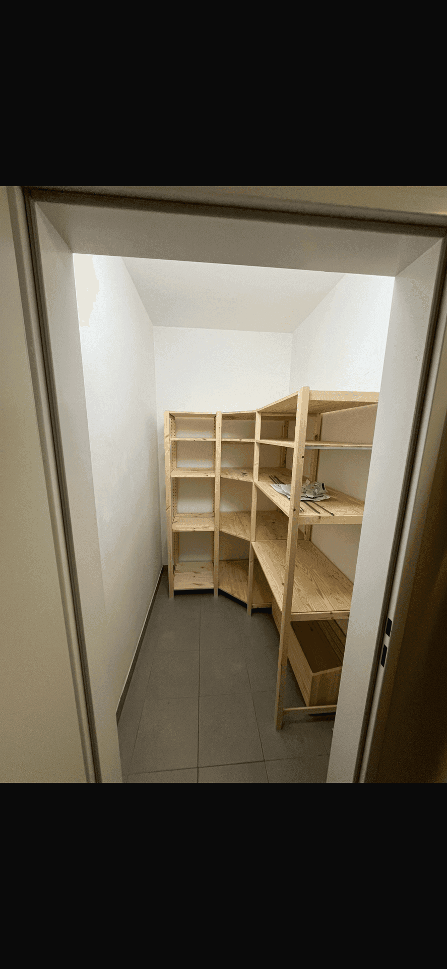 Praktischer Abstellraum mit Holzregalen und Fliesenboden für zusätzlichen Stauraum.