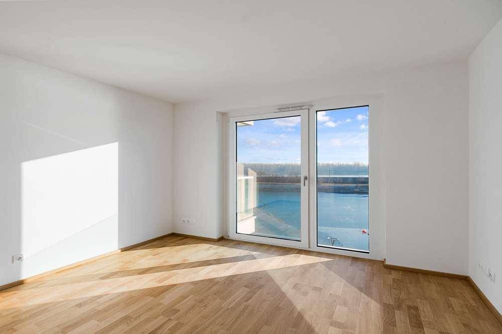 Helles Zimmer mit Holzboden und Zugang zu einem Balkon, der einen weiten Blick bietet.