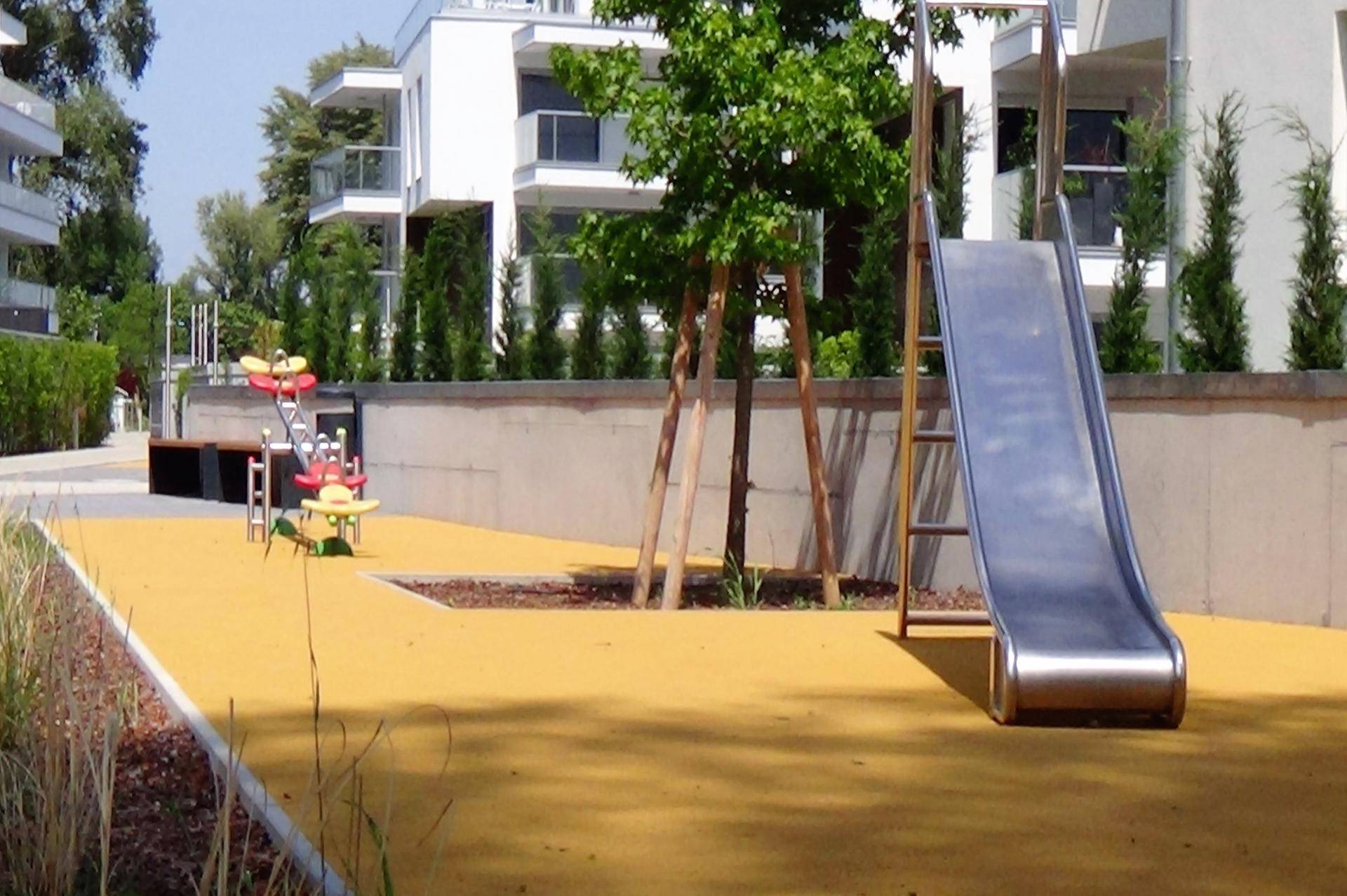Kinderspielplatz mit Rutsche und weichem Untergrund, umgeben von Grünflächen der Wohnanlage.