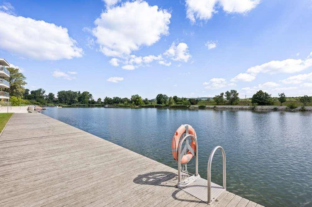 Langer Holzsteg am ruhigen Flussufer mit Rettungsring und Zugang zum Wasser.